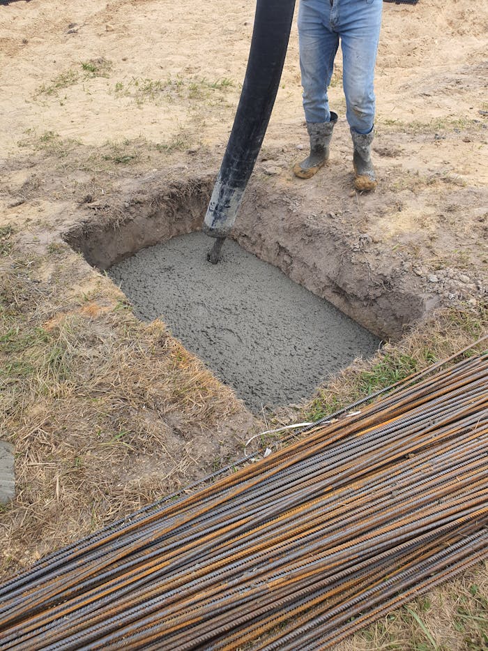 Concrete being poured into a foundation pit at a construction site in Poland, showing rebar and worker boots.