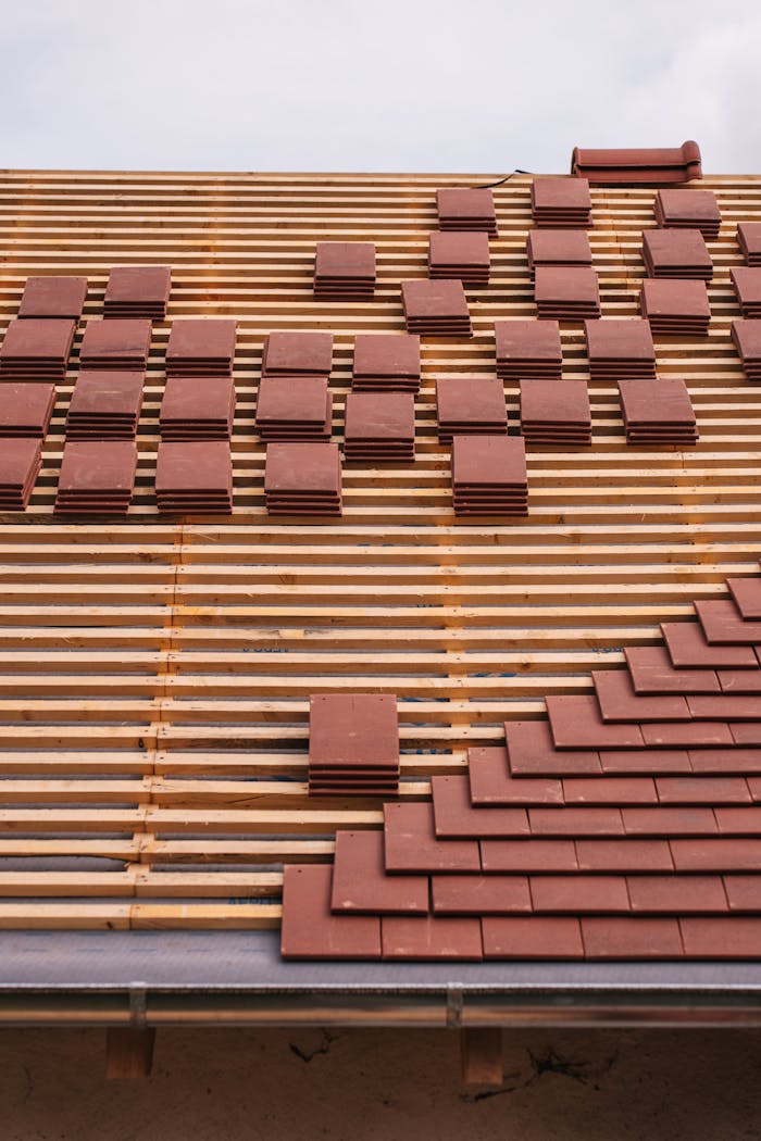 Close-up of red clay tiles being placed on a roof, showcasing construction and craftsmanship.